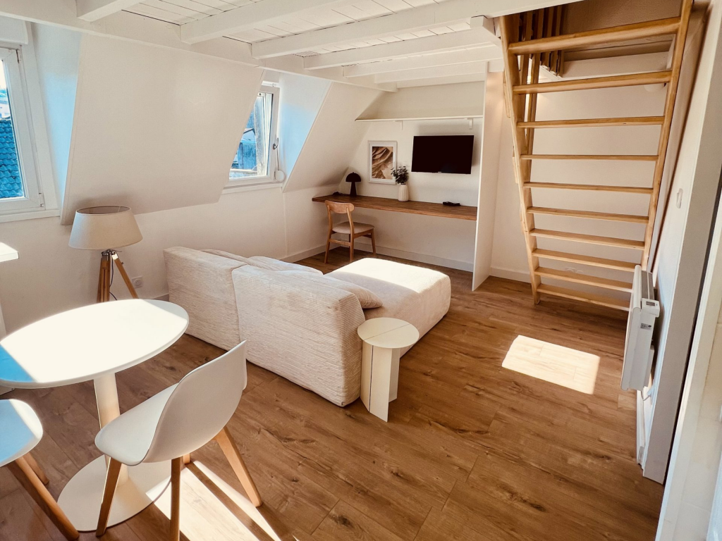 Séjour combles avec canapé beige, escalier échelle bois et bureau