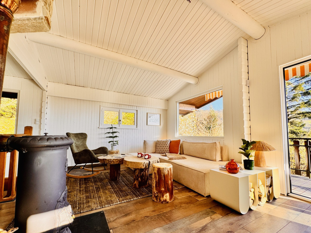 Salon chalet en bois avec poêle à bois, canapé beige et tables en rondins
