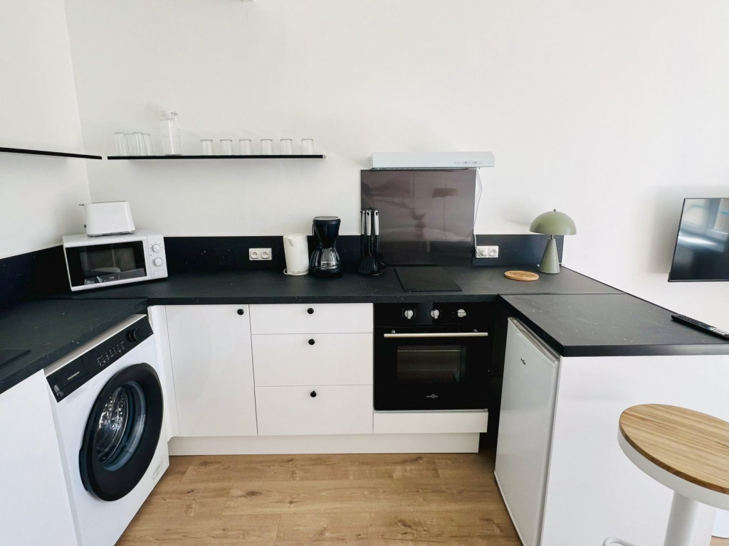 Cuisine blanche équipée avec plan de travail noir, four et lave-linge