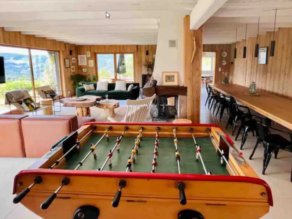 Beau séjour avec babyfoot, grande table à manger en bois avec chaises en métal noir et grande baie vitrée