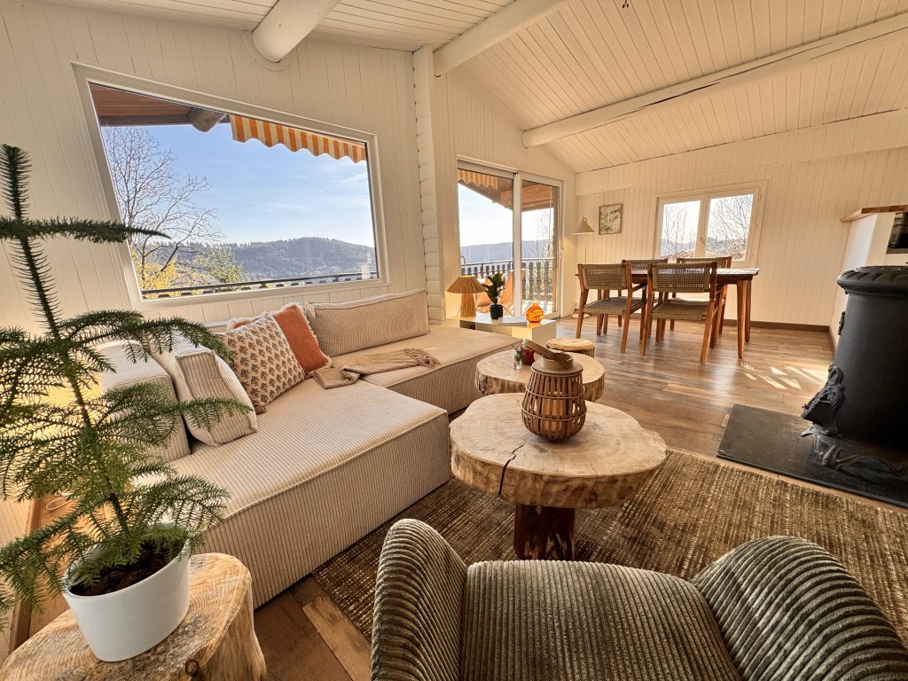 Salon séjour lumineux avec vue montagne, canapé et fauteuil en velours, table basse en bois massif